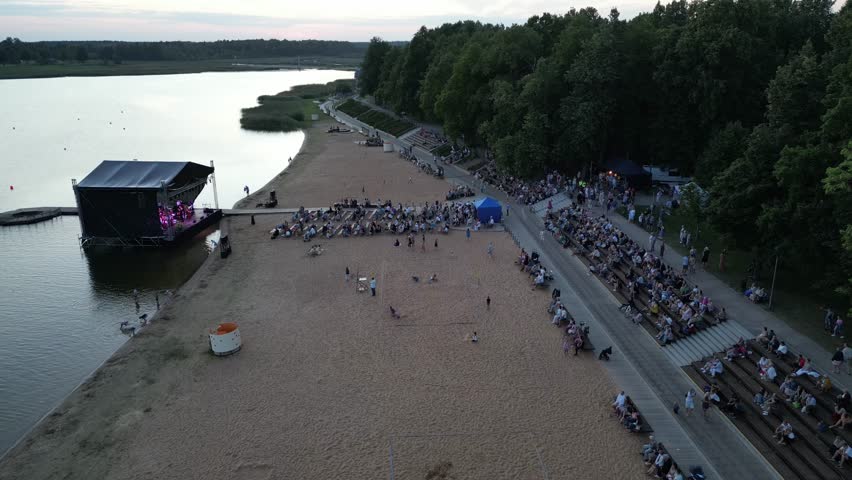 A large crowd of people at a music festival in open air. Concert nearby the lake. Festival concert at summer evening. Street music big event, Stadium on water. Open-air music festival. Estonia