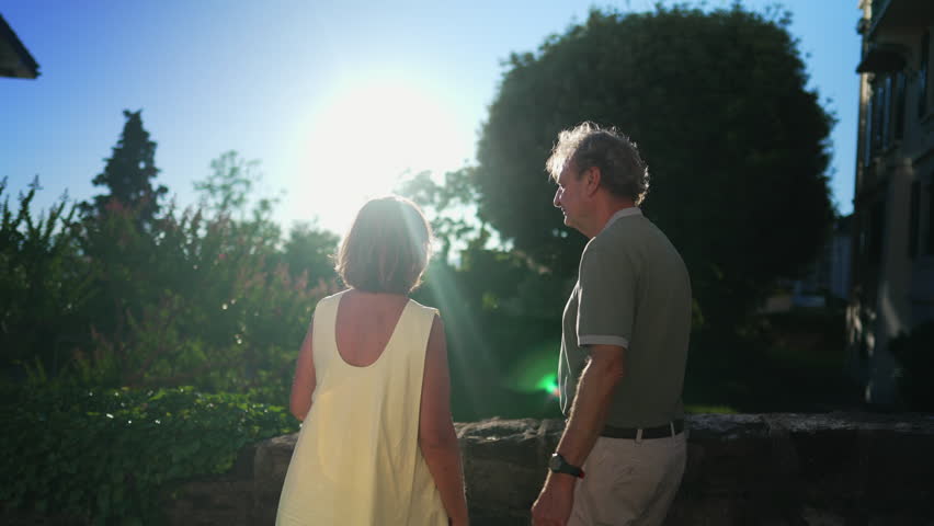 Romantic senior couple looking at sunset together. Senior husband with arm around wife standing outdoors at park