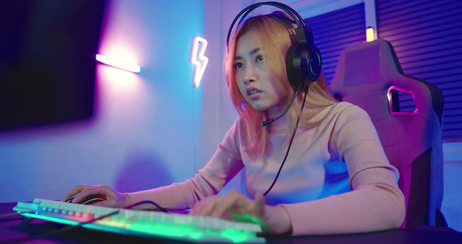 Young player woman wearing gaming headphones intend to do playing live stream games online at home, Happy Gamer endeavor plays online video games tournament with computer desktop with neon lights Royalty-Free Stock Footage #1100177371
