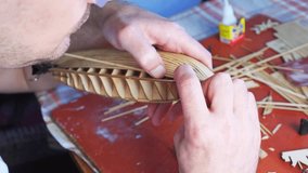 Hands of man gluing plywood details for ship model with glue, holding with fingers. Process of building toy ship, hobby, handicraft. Table with various materials, parts and devices for work. 4k video