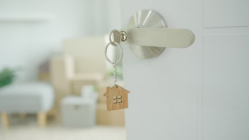 Moving house, relocation. The key was inserted into the door of the new house, inside the room was a cardboard box containing personal belongings and furniture. move in the apartment or condominium | Shutterstock HD Video #1100183039