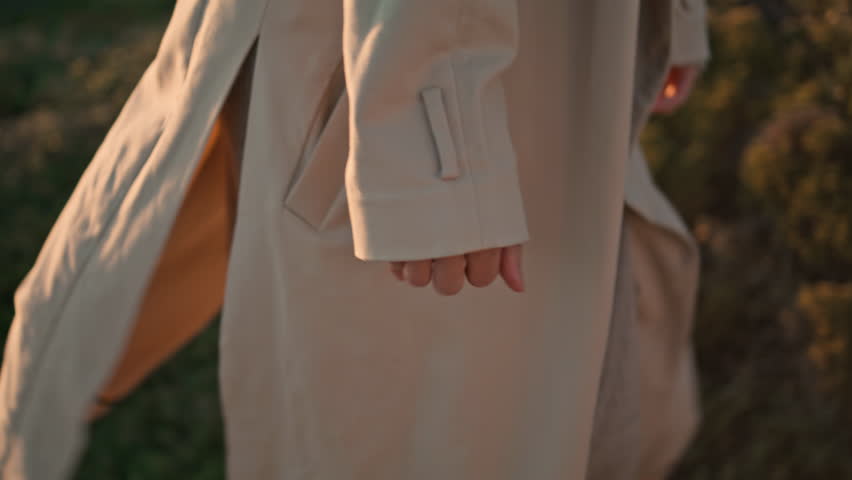 Closeup girl body going green hill in beige coat. Serene woman hiking evening landscape admiring nature at sunset. Beautiful curly female look camera enjoy weekend outdoors. Travel leisure concept