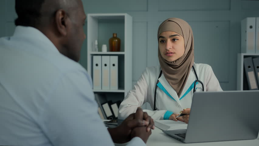 Medical consultation in clinic female doctor cardiologist arabian woman give professional advice to sick patient old man write prescription notes in notebook filling health insurance writing diagnose Royalty-Free Stock Footage #1100187037