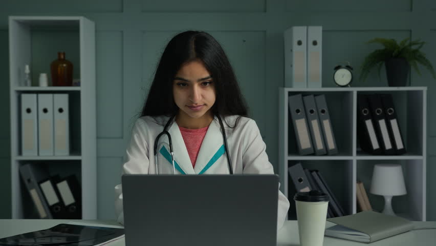 Happy positive woman doctor arabian indian ethnic therapist physician working with laptop looking at camera smiling show okay hand gesture recommend good result approve health care medical insurance Royalty-Free Stock Footage #1100187075