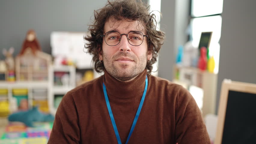 Young hispanic man preschool teacher smiling confident doing ok gesture at kindergarten