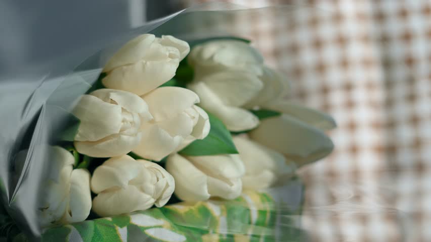 Close-up of a bouquet of white tulips. White tulips lie in a decorative white wicker basket on a wooden table near the window | Shutterstock HD Video #1100190903