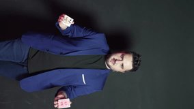 Vertical video of a young magician in the dark throwing two decks of cards in front of him with both hands while smiling and looking at the camera. - Powered by Shutterstock - Get 15% off with code: PIKWIZARD15
