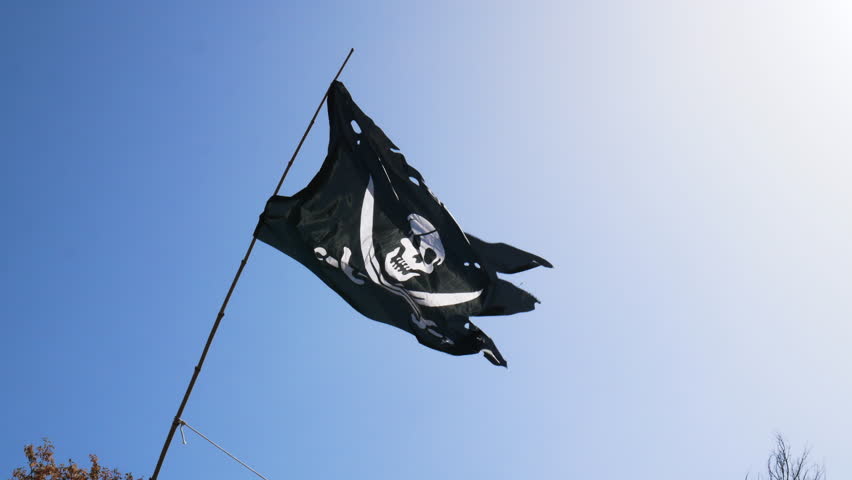 Completely torn and bruised black colored pirate flag (Jolly Roger) fastened to a flagpole flutters in the wind with a skull with patch and two swords on the bottom in white drawn on the fabric Royalty-Free Stock Footage #1100194869