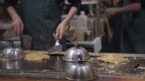 This video shows a restaurant cook frying okonomiyaki on a flat top.