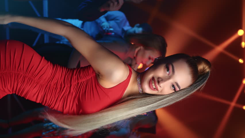 VERTICAL VIDEO POV blonde fashion woman dancing at nightclub party crowded illuminated dance floor. Glamour female dancer in red dress posing at discotheque flashlight relaxing music weekend leisure | Shutterstock HD Video #1100198335