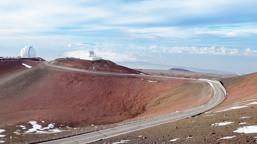 Astronomic telescopes on Mauna Kea summit at sunset on Big Island, Hawaii state in USA. Top of Mauna Kea mountains with international science Observatories on top of red volcanic surface above clouds