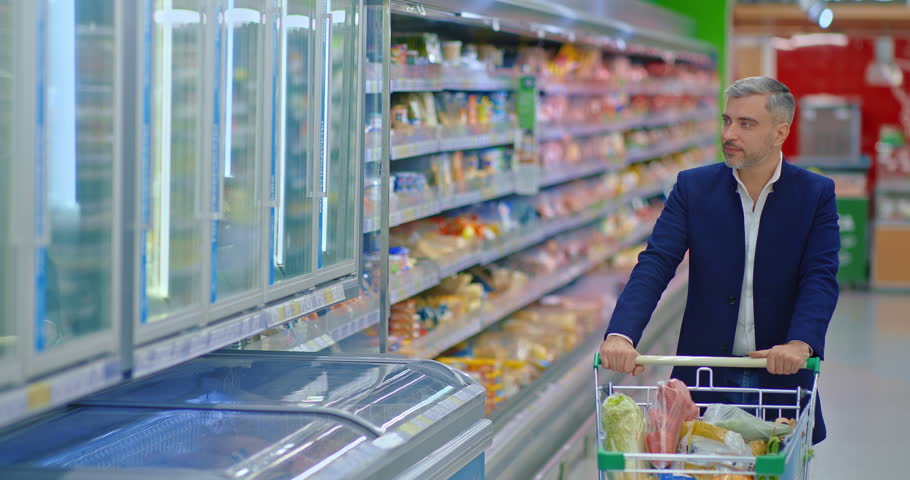 grey-haired man walking in trading floor of supermarket, rolling shopping cart, portrait, 4K, Prores
