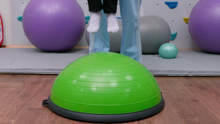 Kid legs jumping on ball on sensory integration session. child girl in rehabilitation centre with physiotherapist doing orthopedic correction. close up  Royalty-Free Stock Footage #1100199725
