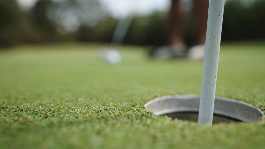 Closeup shot of asian Thai young male golfer tapping the golf ball into a hole at golf course