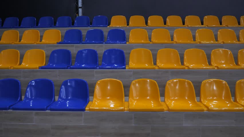 Plastic seats in yellow and blue color on the wooden podium of the stadium, close-up