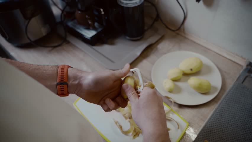 Hands close-up a man peels potatoes with knife in kitchen at home. Cooking, healthy eating. Process cleaning vegetables. Healthy meal. Peeling fresh yellow potato kitchen peeler. Food preparation.
