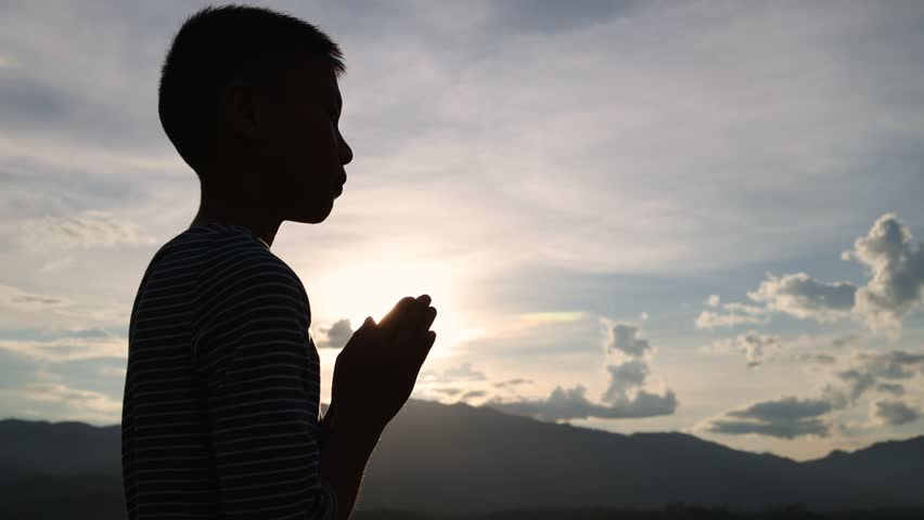 silhouette of boy praying for the sun going down concept spirituality and religion , faith. Religious beliefs. .God