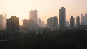 Glowing orange sun setting behind city buildings in silhouette. Colorful sunset behind the high-rise building and skyscrapers of the Mumbai city skyline in India. Timelapse video