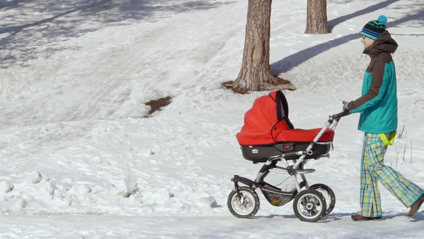 Young beautiful mother walking with a baby bassinet stroller in city park at winter. 
Spending time with newborn and breathing fresh air. Enjoying peaceful stroll.
Happy motherhood concept.  Royalty-Free Stock Footage #1100211591