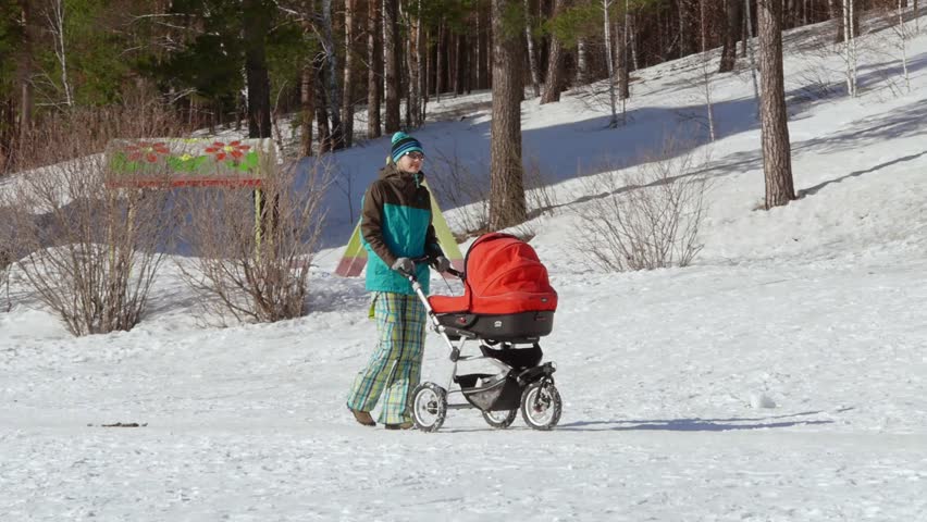Young beautiful mother walking with a baby bassinet stroller in city park at winter. 
Spending time with newborn and breathing fresh air. Enjoying peaceful stroll.
Happy motherhood concept.  Royalty-Free Stock Footage #1100211593