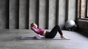A woman performs a myofascial release for her back using a roll on a yoga mat. 