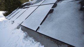 4k video with some solar panels covered with snow next to a mountain cottage in a winter morning. Photovoltaic energy industry.