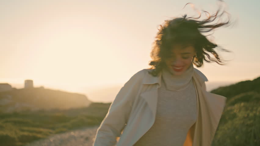 Happy girl going sunset seashore rear view. Cheerful woman rejoicing in sunlight enjoying wonderful life at ocean mountain evening. Curly satisfied silhouette walking spinning chill in quiet place. 