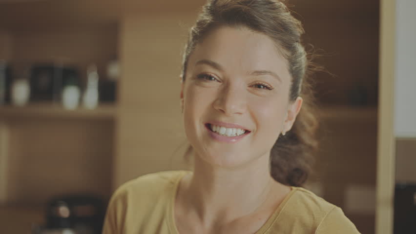 Portrait shot of a beautiful woman standing alone in the kitchen and smiling while looking at camera in slow-motion | Shutterstock HD Video #1100225767