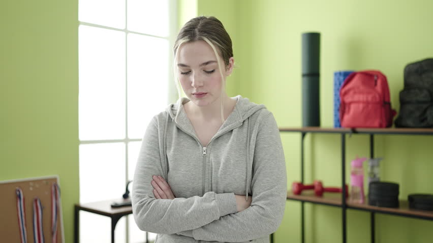 Young blonde woman standing with relaxed expression at sport center