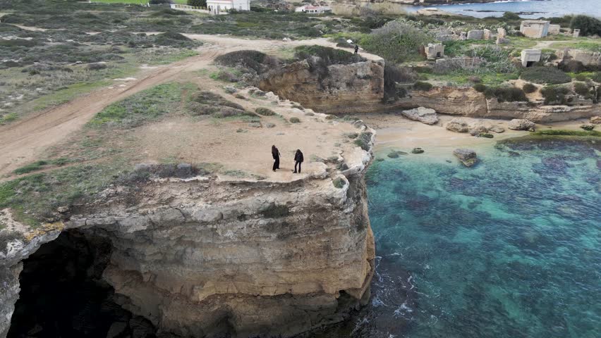 Aerial view of two person standing on white cliffs at Pillirina cave on Plemmirio natural reserve, Syracuse, Sicily, Italy.