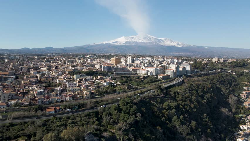 Aerial view of Acireale along the coastline with Etna Volcano during eruption in background, Catania province, Sicily, Italy.
