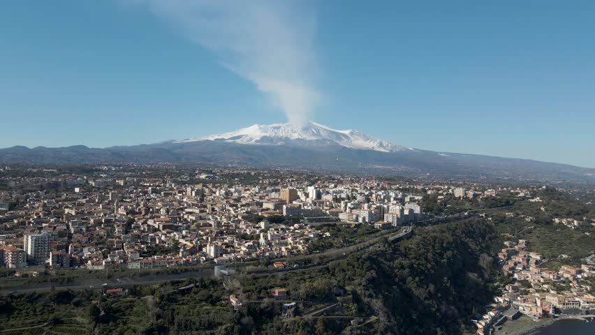 Aerial view of Acireale along the coastline with Etna Volcano during eruption in background, Catania province, Sicily, Italy.