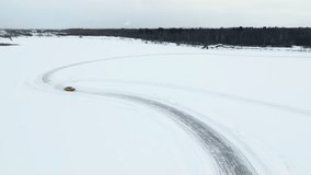 Aerial view of a driving car at snowy track at winter. Clip. One car driving through ice covered lake.