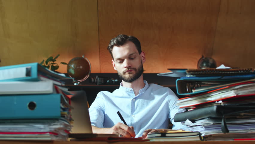Happy young Caucasian businessman works at modern office table signing documents, leaning back finishing work. | Shutterstock HD Video #1100237893