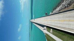 Vertical drone shot of Florida Keys bride, moving the video forward and capturing the bridge above blue Atlantic Ocean water on a sunny and shiny day when the skies are clear and blue.