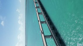 Vertical drone shot of Florida Keys bridge, moving the video sideways and capturing the bridge above blue Atlantic Ocean water on a sunny and shiny day when the skies are clear and blue.