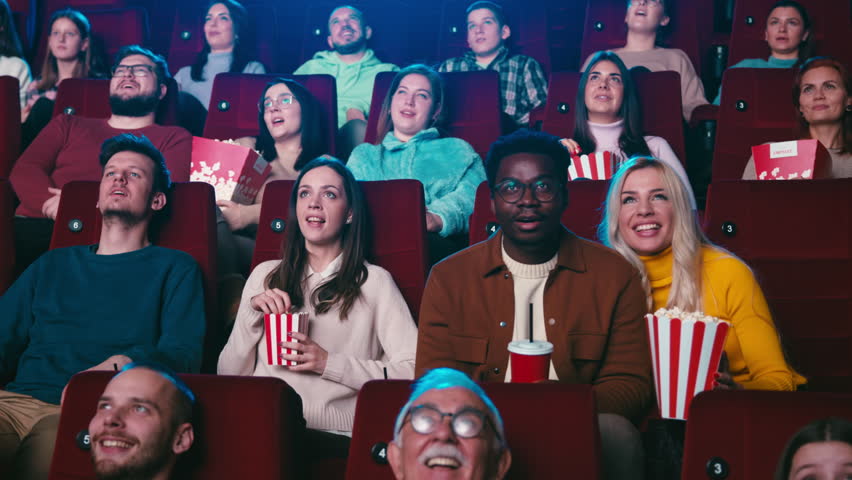 A movie theater full with diverse audience watching an exciting movie on the big screen and eating popcorn. Royalty-Free Stock Footage #1100239809