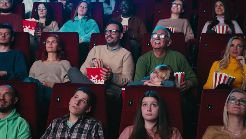 A diverse audience in a movie theater having fun while watching a movie and enjoying popcorn. | Shutterstock HD Video #1100239875