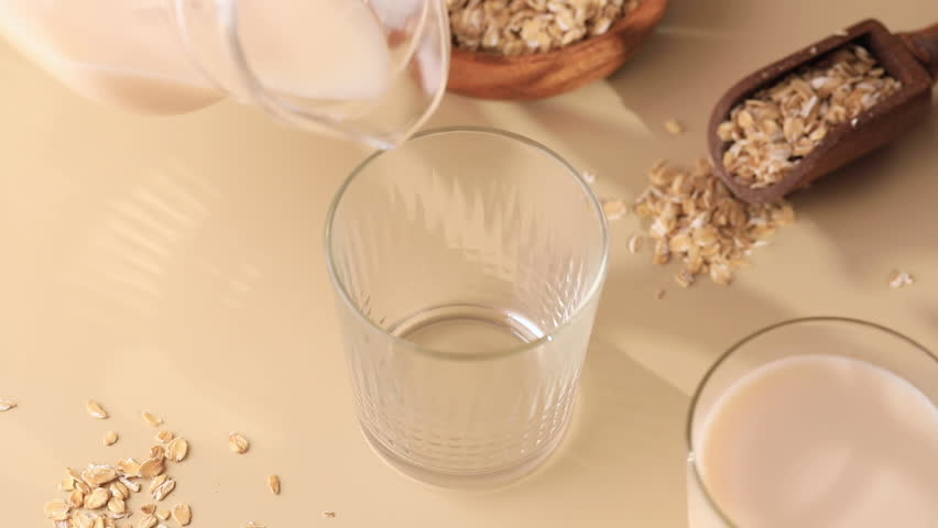 Oatmeal vegetarian milk is poured into a glass from a jug. Alternative milk | Shutterstock HD Video #1100240433