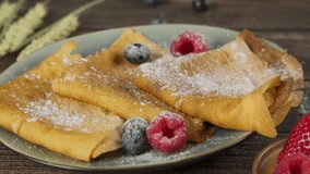 Pouring chocolate sauce on folded French crepes, thin pancakes served on plate with fresh blueberries and raspberries, tasty Russian pancakes, high quality video, slow motion 4k footage