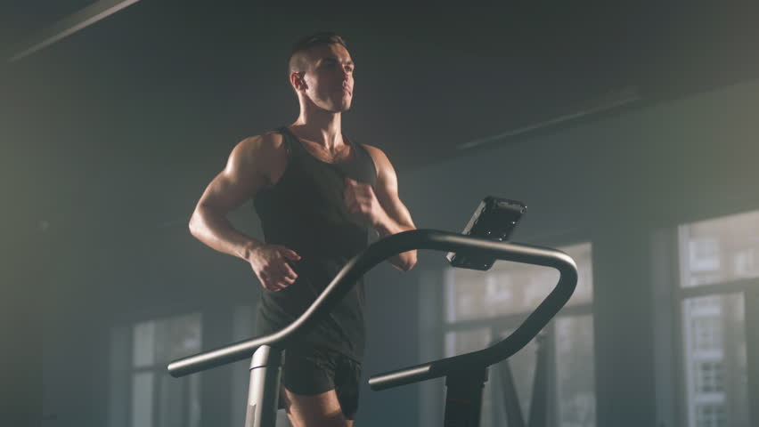 Close-up view of active, caucasian sportsman having intensive cardio workout to burn calories. Portrait of young, caucasian man jogging on gym machine. High quality 4k footage