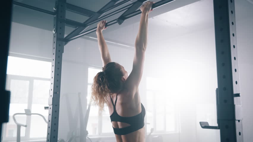 Portrait of a sportswoman practicing intensive workout. Close-up view of female athlete using pull up bar to build impressive upper-body muscle in loft-styled gym studio. High quality 4k footage Royalty-Free Stock Footage #1100242401