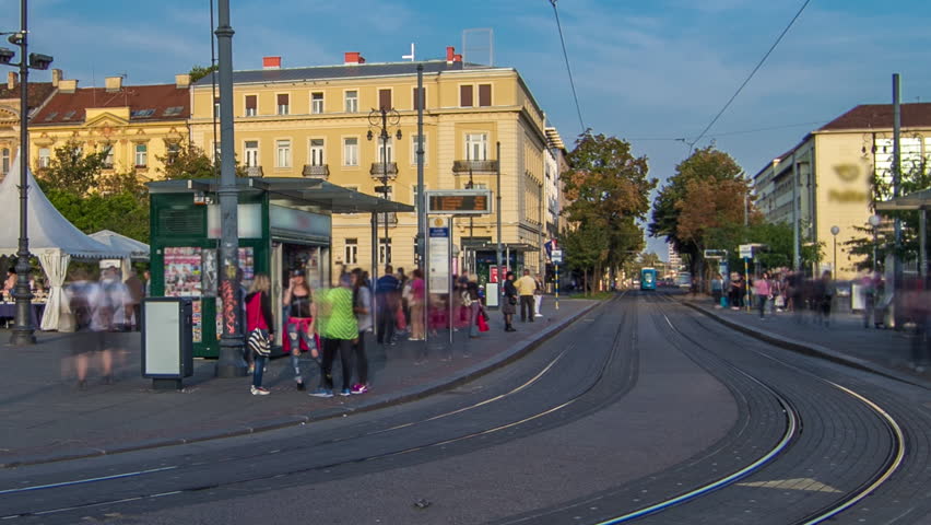 New modern trams of Croatian capital Zagreb timelapse near railway station. People at tram stop at sunset time. CROATIA