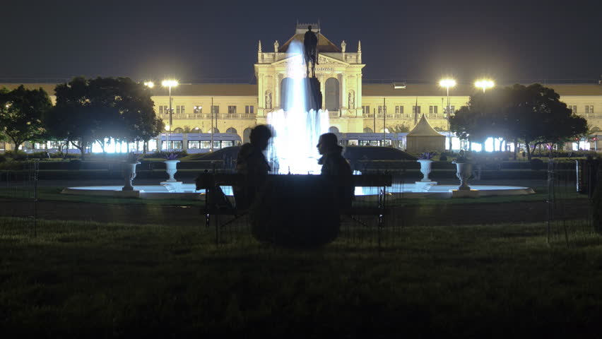 People on the Tomislav Square with fountain in front of Main Railway Station night timelapse, main hub of Croatian Railways network. People on a bench. Zagreb, Croatia