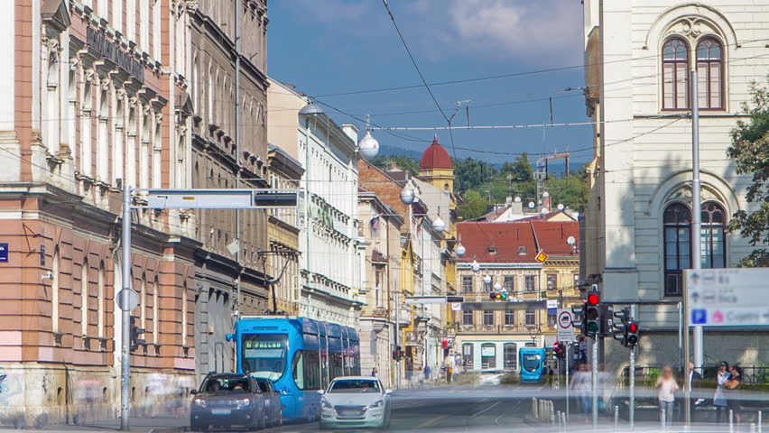 Busy street near new building of Croatian Music Academy timelapse in Zagreb, Croatia. Traffic on the road with trams, blue cloudy sky at sunny day