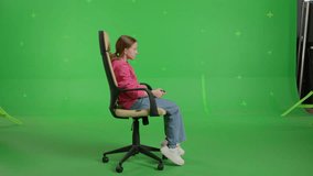 Young caucasian girl sitting on a office chair, Playing in Video Games on a Console. Female gamer using Wireless Controller. Green screen background, chroma key