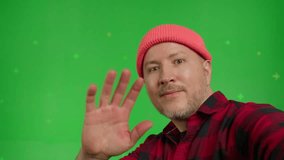 Extreme close-up of a smiling man in shirt and beanie posing on green screen background. Guy taking selfie self portrait photo on smartphone. Chroma key. Male model showing positive face emotions