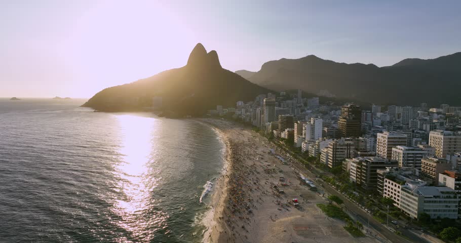 Aerial above Ipanema Beach at sunset, people playing and relaxing on the beach. Sun behind the mountains, Rio de Janeiro | Shutterstock HD Video #1100246577
