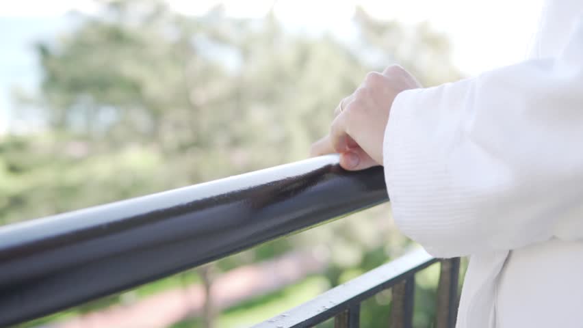 A woman in a white coat stands on the balcony of the hotel, a close-up of a woman