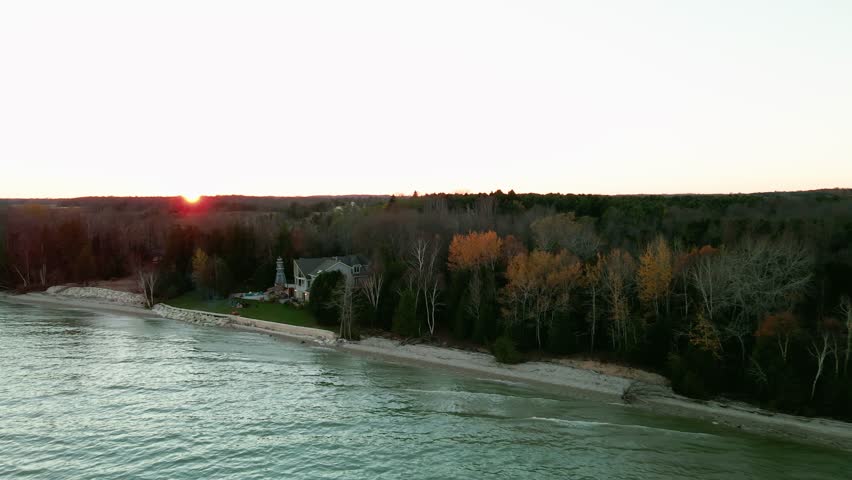 Swooping aerial footage of waterfront mansion, lighthouse, lush trees, and stunning coastal views in Wisconsin. Day, sunset.